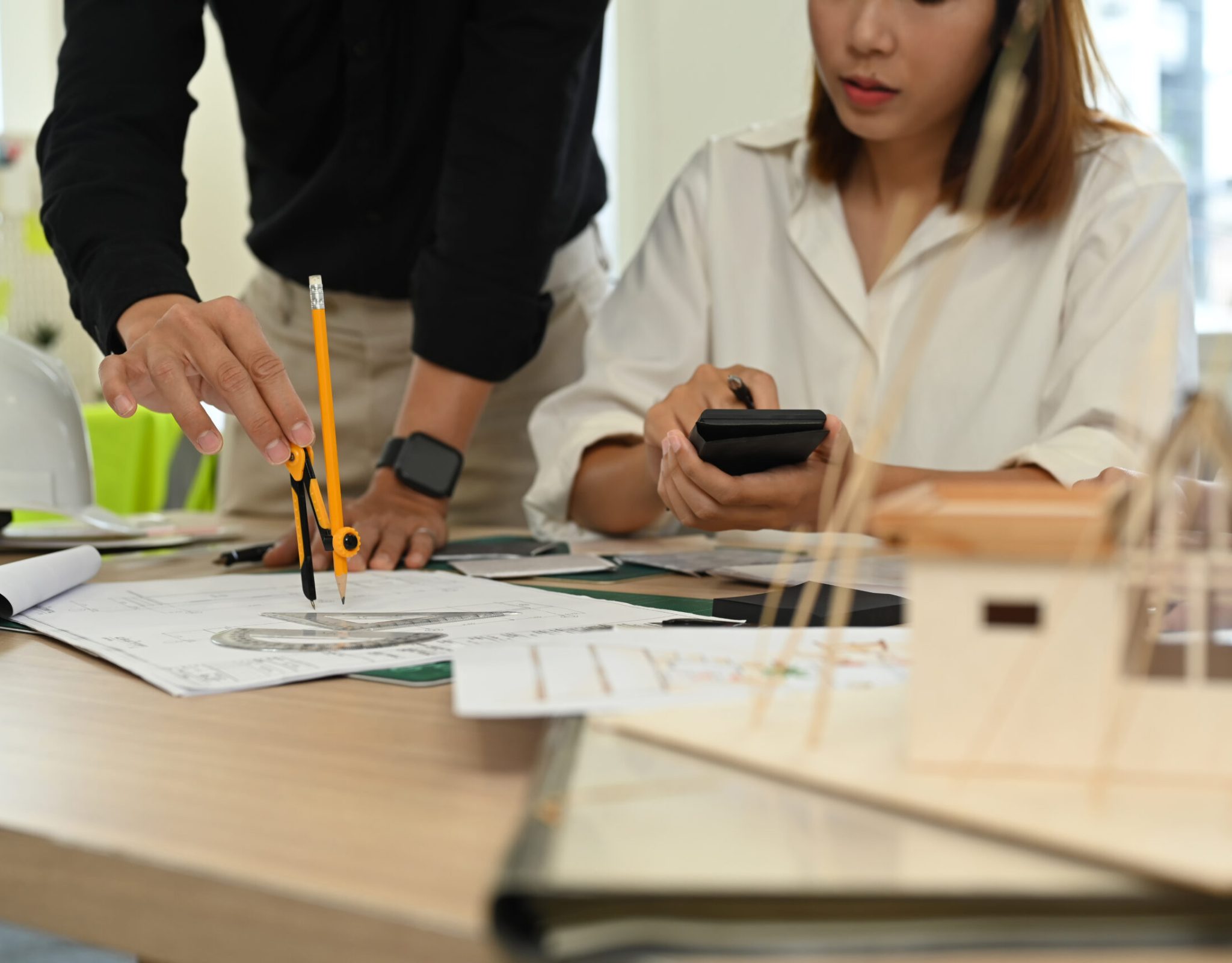 Cropped image of young colleagues working together on architectural project at meeting table.