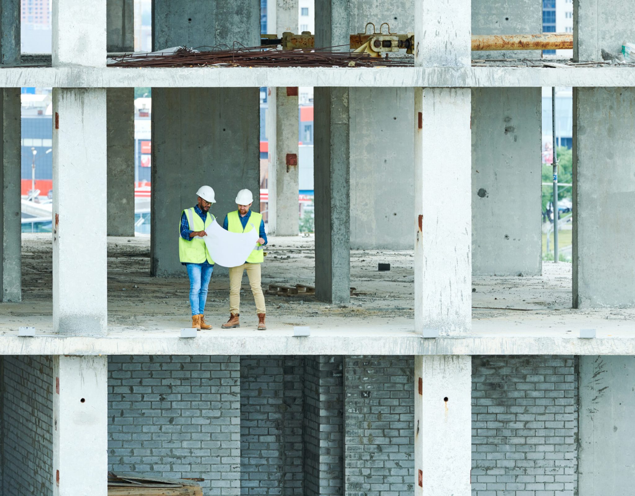 Wide angle view at two builders holding plans standing in unfinished apartment building on construction site, copy space